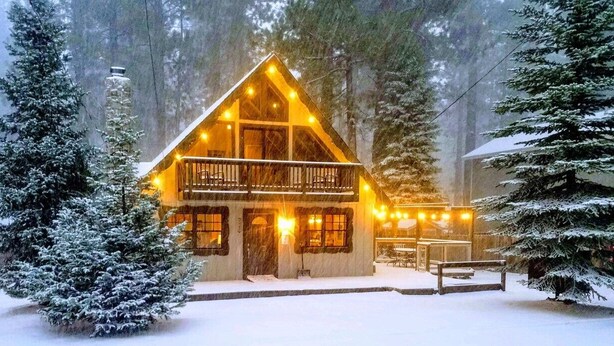A cabin with a balcony, surrounded by snow-covered trees.