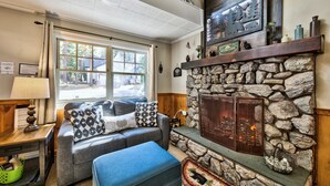 A cozy living room with a stone fireplace, a large window, and a comfortable seating area.