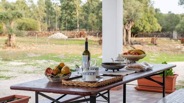 Een terras met een eettafel, gedekt voor een maaltijd, inclusief een fles, kommen en borden.