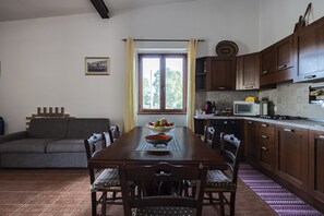 Un espace repas comprenant une table en bois, des chaises, un canapé et une cuisine équipée de placards et d’appareils électroménagers.