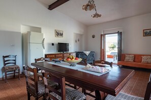 Un coin repas avec une table en bois, des chaises, un panier de fruits, un téléviseur et un canapé.