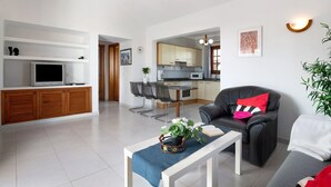 A modern living room with a TV, a dining area, and a kitchen in the background. - Vacation Home 'Casa Aloe' with Sea View, Terrace & Wi-Fi (Haría)