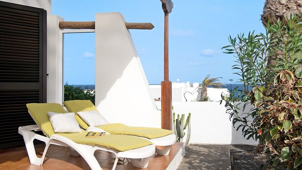 A sunlit outdoor lounge area with white lounge chairs and yellow cushions, a wooden pergola, and a view of the sea. - Vacation Home 'Casa Aloe' with Sea View, Terrace & Wi-Fi (Haría)
