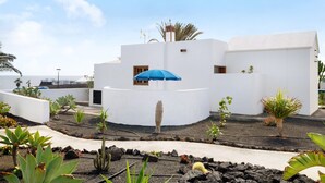 A white building with a blue umbrella, surrounded by various plants and a small cactus. - Vacation Home 'Casa Aloe' with Sea View, Terrace & Wi-Fi (Haría)