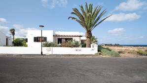 A white building with a palm tree, a lamp post, and a view of the sea. - Vacation Home 'Casa Aloe' with Sea View, Terrace & Wi-Fi (Haría)