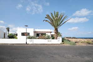 Un bâtiment blanc avec un palmier, un lampadaire et une vue sur la mer.