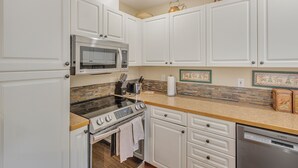 Una cocina con armarios blancos, un microondas de acero inoxidable, una estufa a gas y un lavavajillas Bosch.