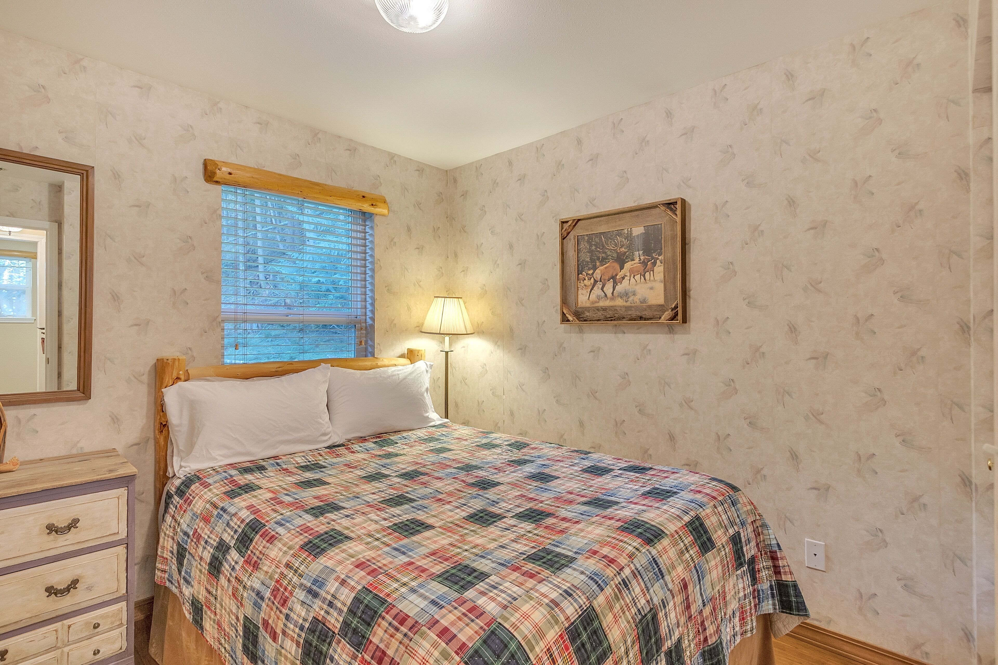 A bedroom with a bed, a nightstand, a lamp, a window with blinds, and a framed picture on the wall.