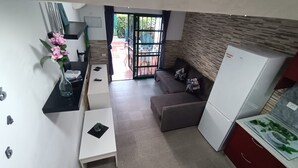 Een knus leefruimte met een kitchenette, een bank, een eettafel en een koelkast.