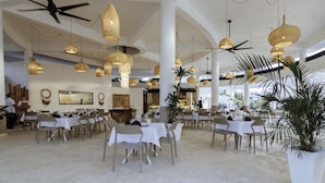 A spacious dining area with multiple tables and chairs, ceiling fans, and hanging light fixtures. - New Beachfront Penthouse by RedAwning (Las Terrenas)