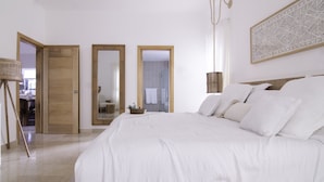 A bedroom with a large bed, wooden doors, a mirror, and a wall-mounted light fixture. - New Beachfront Penthouse by RedAwning (Las Terrenas)