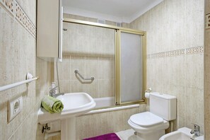 Une salle de bain équipée d’une baignoire, de toilettes, d’un lavabo et d’une douche avec une porte en verre.