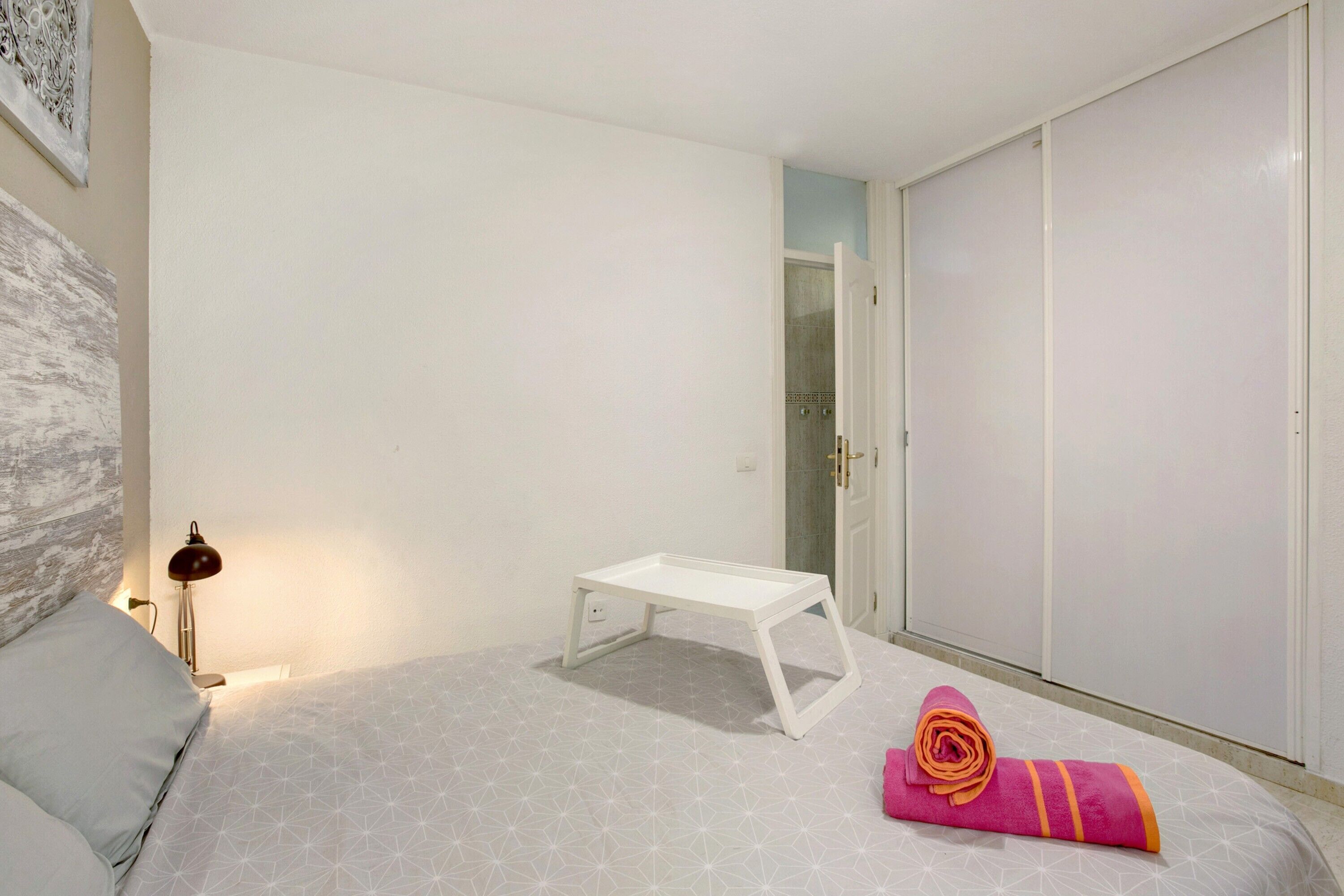 Une chambre à coucher avec un lit, une table de chevet blanche, une serviette enroulée, une lampe et une armoire.