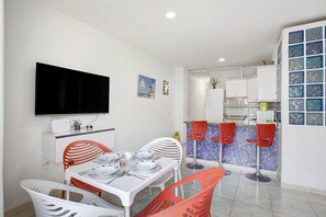 Een kleine keuken met een betegelde spatwand, een flatscreen televisie boven de aanrecht en een eethoek met een tafel en stoelen.