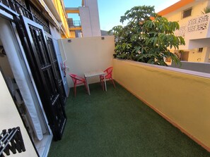 Un petit espace extérieur avec du gazon synthétique, deux chaises en plastique rouge et une table en métal.