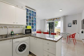 A compact kitchen with a washing machine, microwave, and a small dining area with red chairs. - Vacation Rental 'Apartamento Caletillas Alan' with Shared Pools, Terrace, and Wi-Fi (Candelaria)