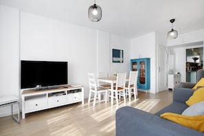 A modern living room with a flat-screen TV, white furniture, and a dining area.