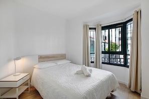 A neatly arranged bedroom with a bed, bedside lamp, and a window with curtains.