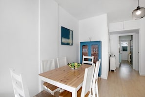 A dining area with a wooden table and white chairs, a blue cabinet, and a white wall with a painting.