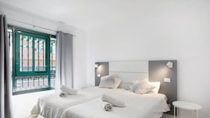 Ein Hotelzimmer mit zwei Betten, einem kleinen weißen Tisch und einem Fenster mit Blick auf ein Gebäude.