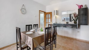 Un coin repas avec une table dressée pour quatre personnes, des chaises, une horloge murale, un miroir et un buffet.