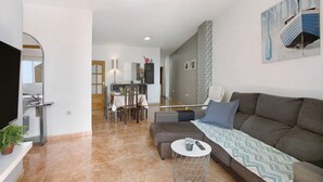 Un salon moderne avec un canapé, une table basse, un téléviseur et, au fond, un coin repas.