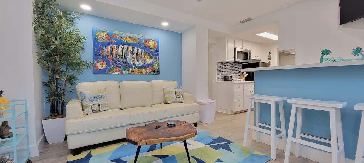 A living room with a sofa, a coffee table, a plant, and a colorful painting on the wall.