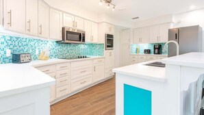 Una cocina moderna con armarios blancos, salpicadero de azulejos azules, electrodomésticos de acero inoxidable y suelo de madera.
