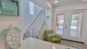 Una escalera que sube a un segundo piso, una silla verde y una puerta con un panel de vidrio.