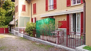 Un edifici de dues plantes amb persianes vermelles, una caixa d'ús general verd i una tanca metàl·lica.
