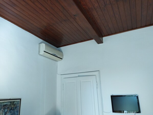 Une pièce avec un plafond en bois, une porte blanche et un téléviseur fixé au mur.