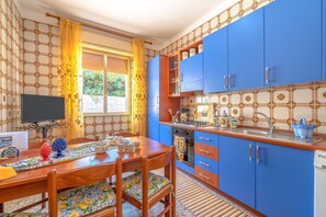 Une cuisine avec des meubles de rangement bleus, une table à manger en bois et un téléviseur.