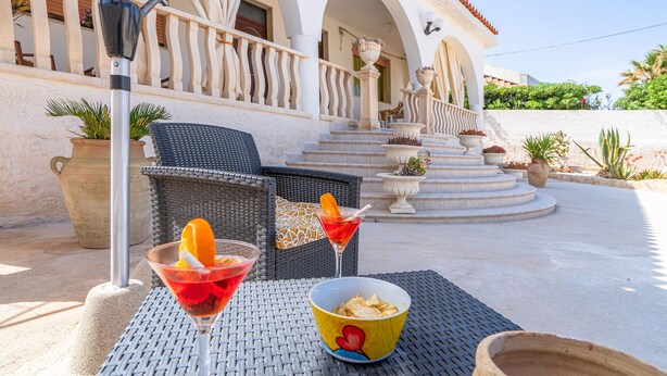 An outdoor seating area with wicker chairs, a table, and a bowl of chips.