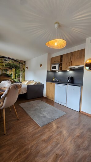 Habitación compacta y moderna con cama, zona de comedor, kitchenette y vista a un pequeño jardín.