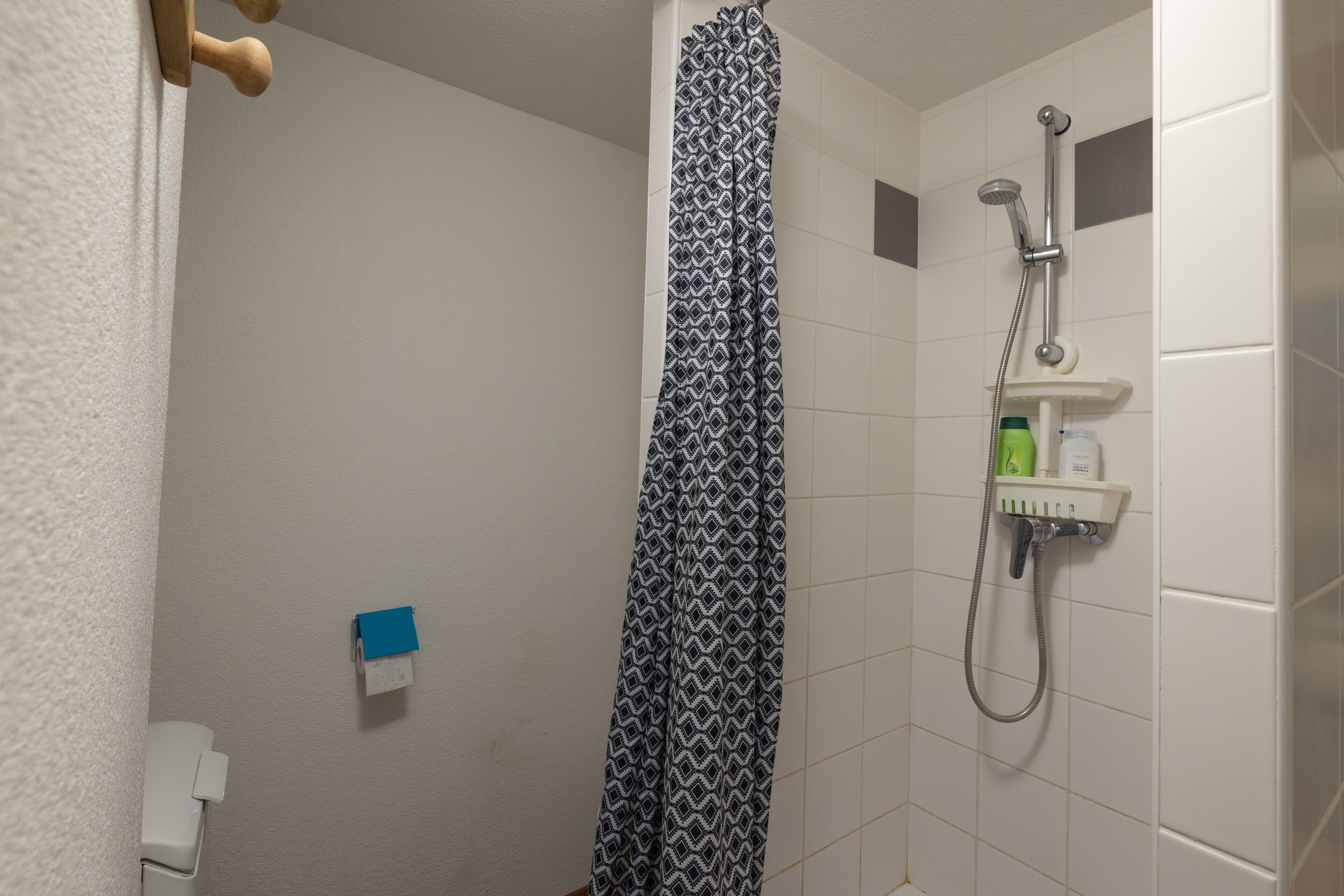 Ducha con cortina estampada, cabezal de ducha de mano y dispensador de jabón en un estante fijado a la pared.