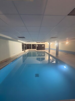 An indoor swimming pool with clear water, a tiled floor, and a ceiling with recessed lighting.