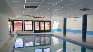 An indoor swimming pool with clear water, tiled walls, and a view of the outside through large windows. - '12 MN Megève Studio Comfort' with Mountain View (Flumet)
