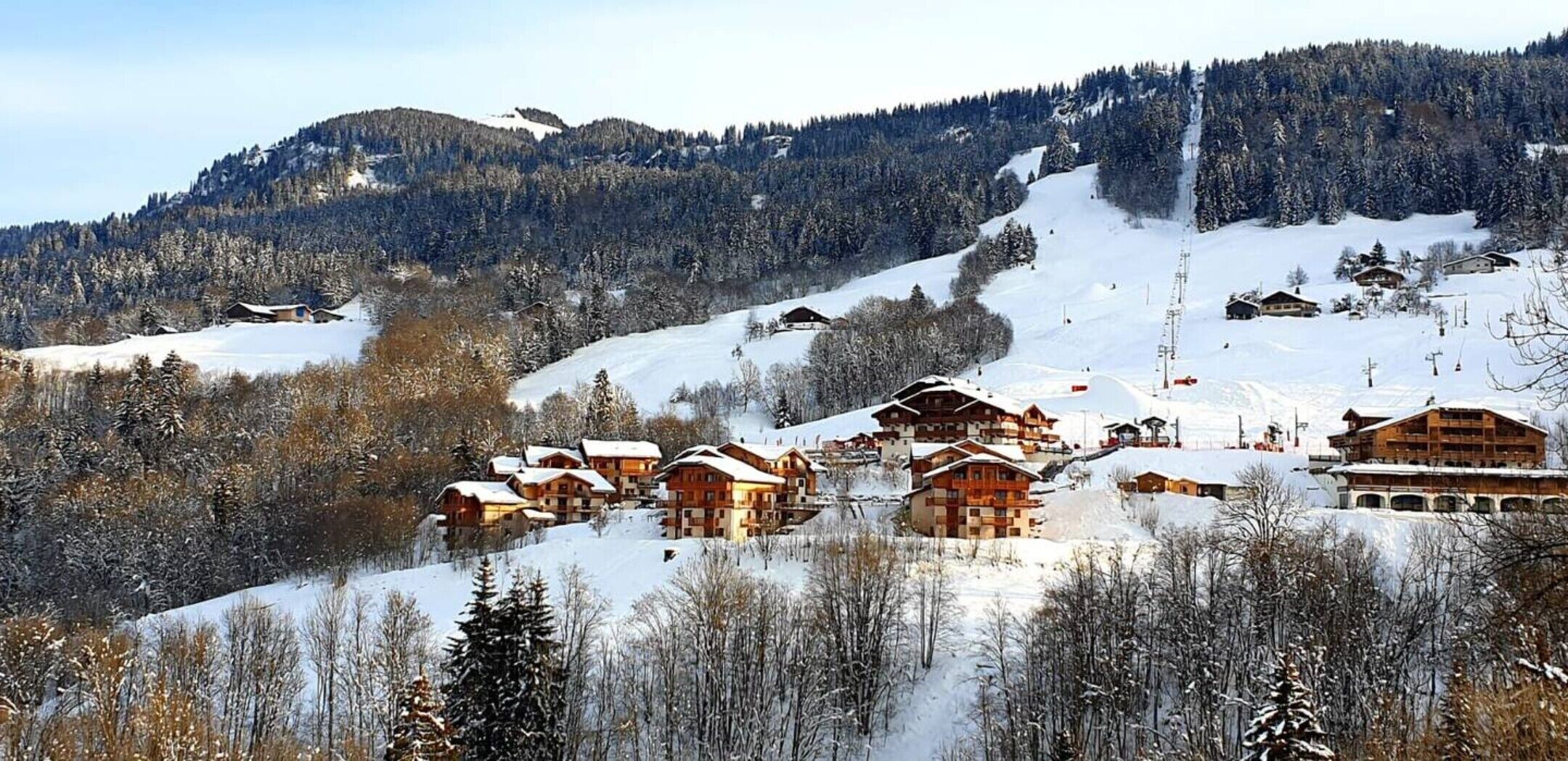 Un village de montagne enneigé, avec des chalets en bois, des pistes de ski et un télésiège.