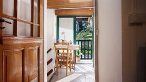 Una porta in legno con pannelli di vetro, una sedia in legno, un tavolo con tovaglia fiorita e una porta verde che dà su un balcone con ringhiera.