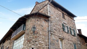 Un edificio in pietra con un balcone, una finestra con persiane e un camino.