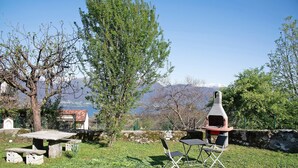 Un tavolo e sedie in pietra in un'area verde all'aperto, con un forno a mattoni e vista sulle montagne.