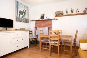 Eine Küche mit Fernseher, Holzstühlen, einem Esstisch, einem Kamin und einem Regal mit Pflanzen.