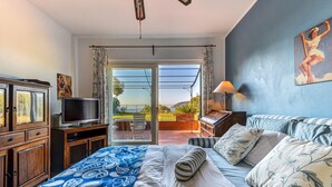 Une chambre avec un lit, une télévision, un bureau et une vue sur l’extérieur, visible à travers une porte vitrée.
