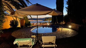 Un espace piscine extérieur avec une table et des chaises, un coin salon couvert et une vue sur la mer.