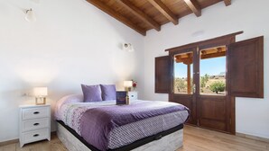 Ein Schlafzimmer mit einem Bett, Holzboden, weißen Wänden, einem Nachttisch mit Schubladen, einer Lampe und einem Fenster mit Blick.