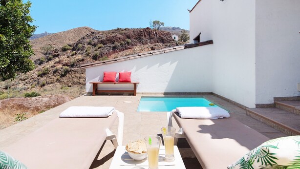 Ein Poolbereich mit Liegestühlen, einem Tisch mit Getränken und Blick auf einen Berg.