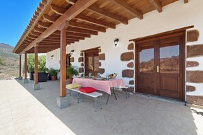 A covered patio with a table set for dining, stone walls, wooden doors, and a mountainous backdrop. - Accessible Holiday Home 'El Algarrobero' with Mountain Views and Private Pool (Rosiana)
