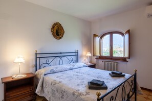 Une chambre à coucher avec un lit, deux lampes de chevet, un radiateur, une fenêtre donnant sur un paysage agréable et un tableau encadré au mur.