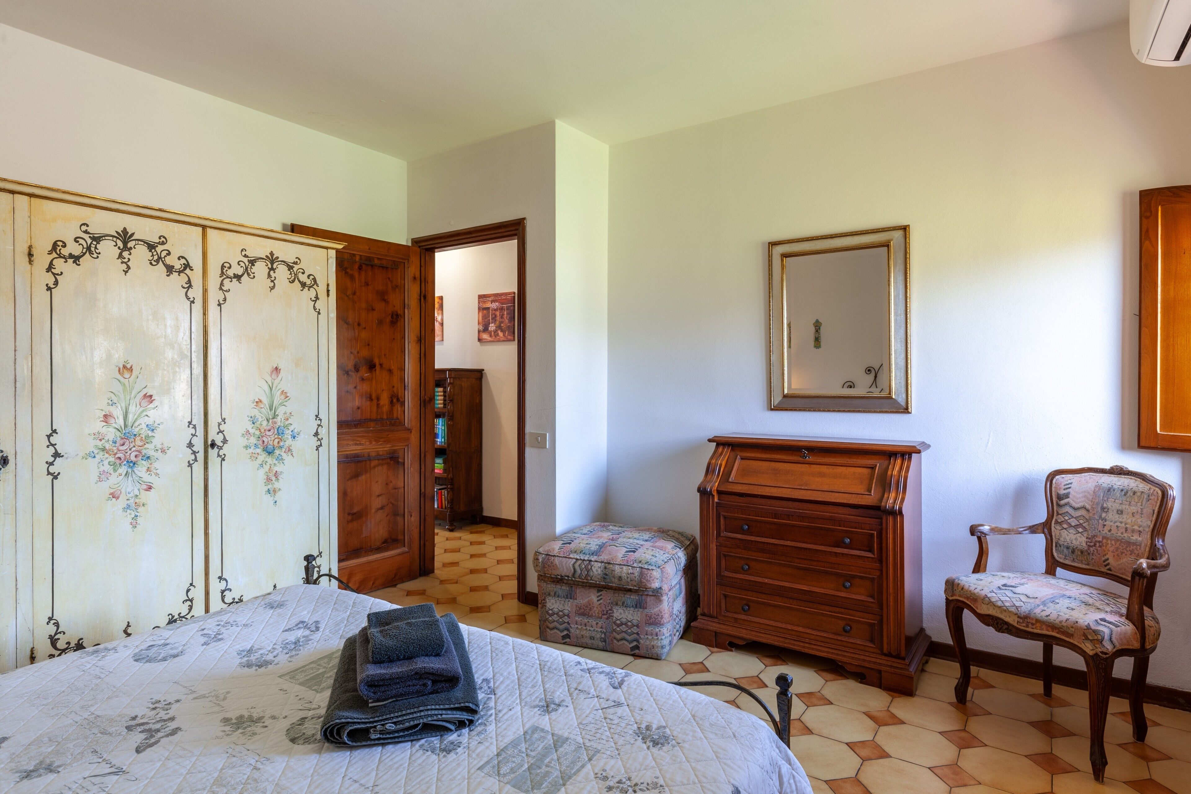 Un dormitorio con cama, armario de madera, cómoda, silla y espejo en la pared.