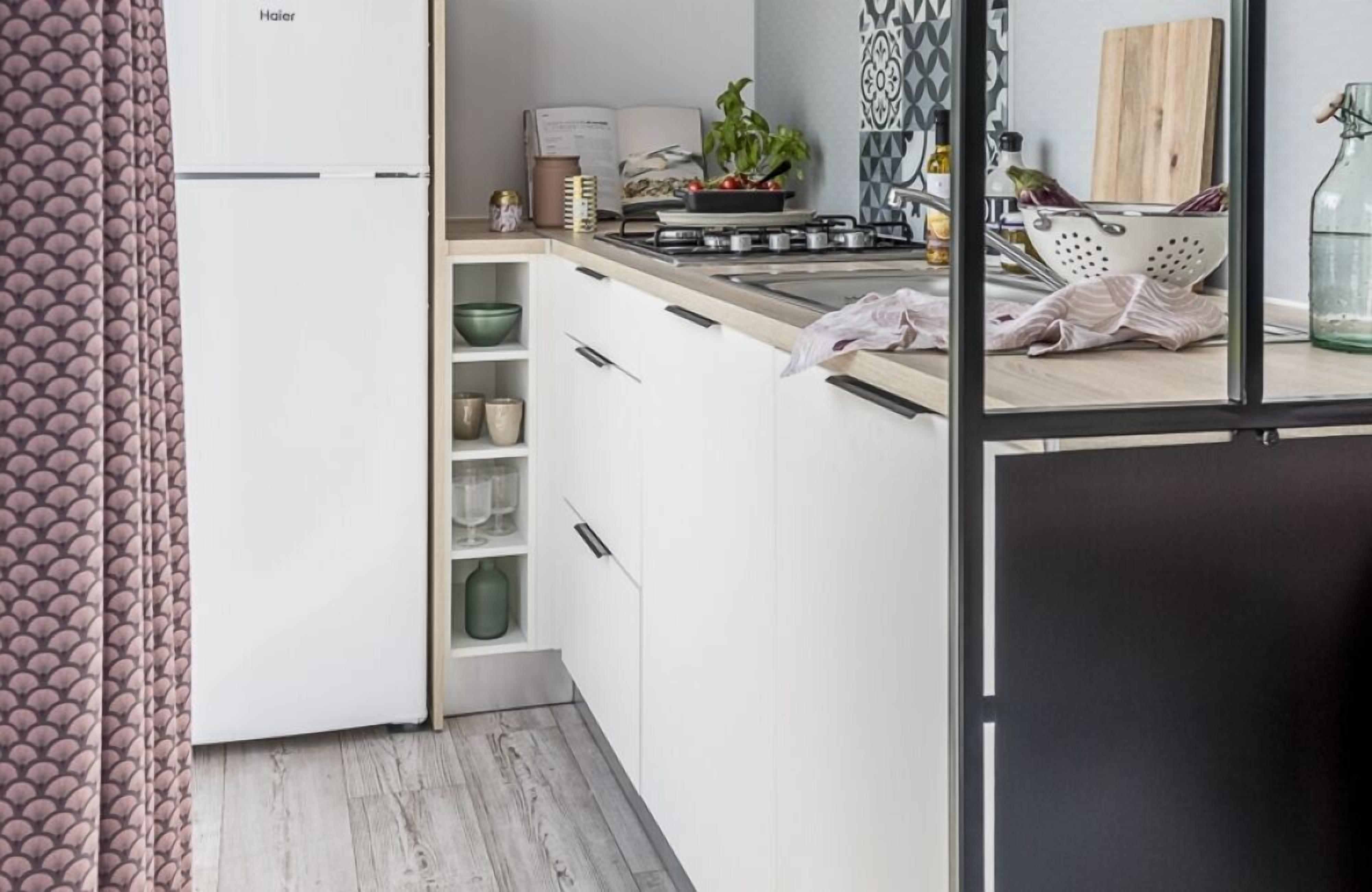 Una cocina moderna con armarios blancos, una estufa y un lavabo. Hay una planta en la encimera y una tabla de cortar de madera.